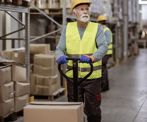 An older employee driving a pallet jack in a warehouse.