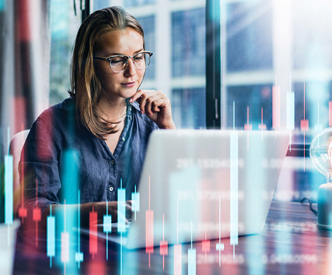 A woman sitting and working with visualizations of data tables around her.