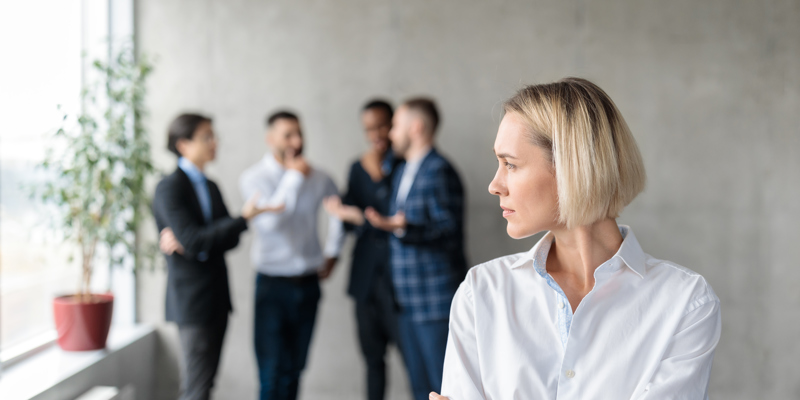En kollega der står alene og kigger mod en gruppe andre kolleger der snakker sammen