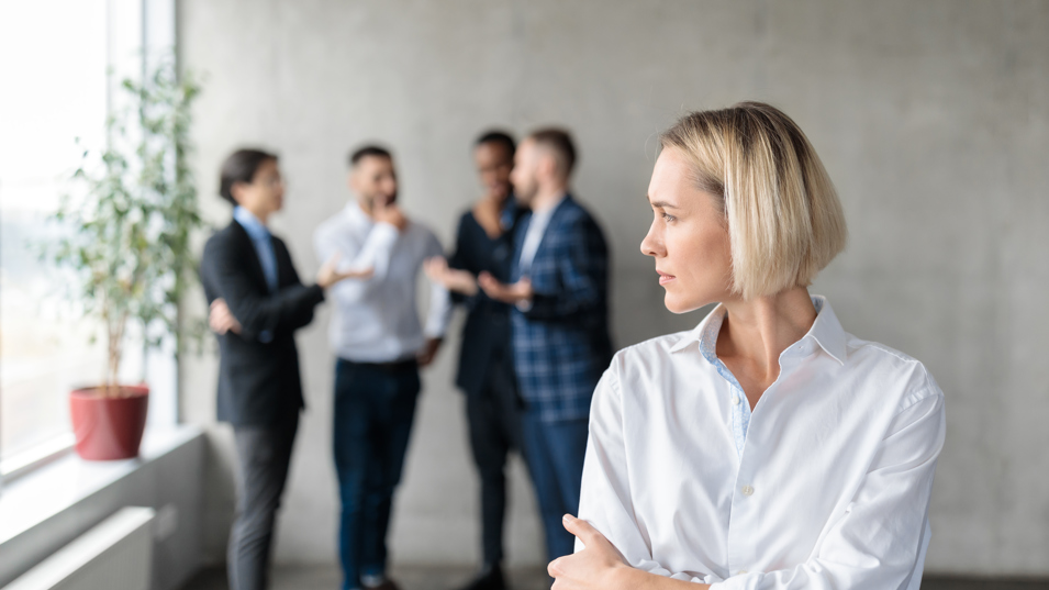 En kollega der står alene og kigger mod en gruppe andre kolleger der snakker sammen