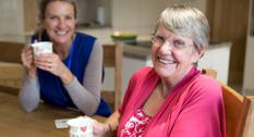 En hjemmehjælper der sidder og drikker kaffe med en senior