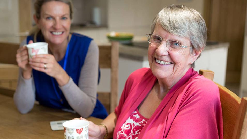 En hjemmehjælper der sidder og drikker kaffe med en senior