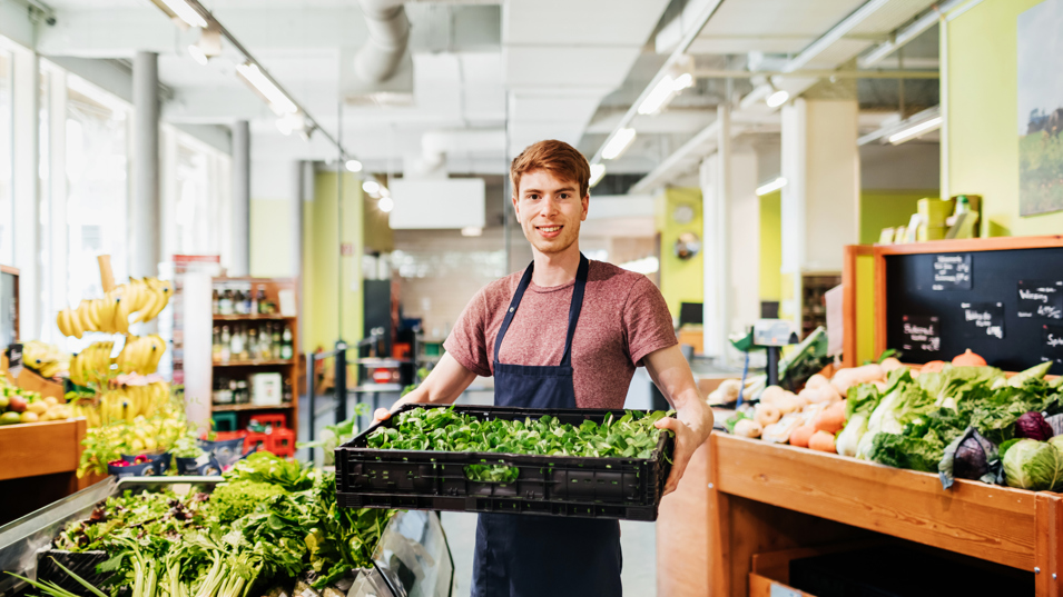 Ansat i grøntafdeling i et supermarked, der holder en kasse med grøntsager
