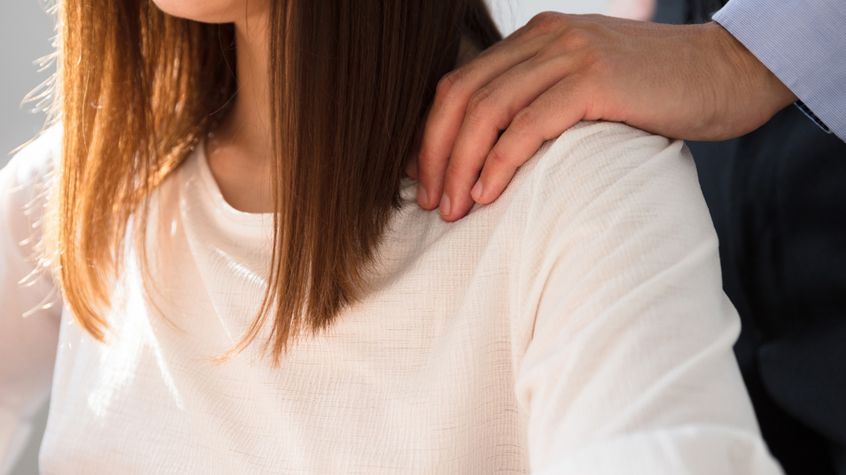 En mandlig kollega, der lægger en hånd på sin kvindelige kollegas skulder