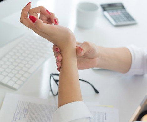 A woman working at a computer is holding her wrist.