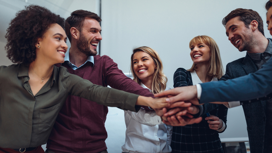 Kolleger der lægger hænderne oven på hinanden og smiler.